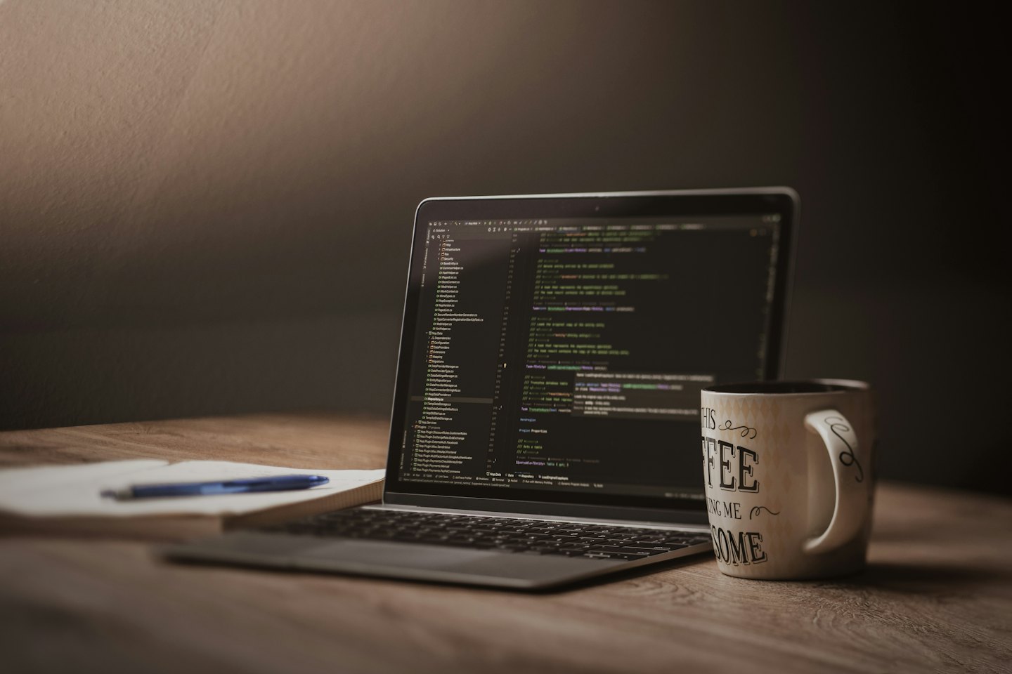 Computer portatile aperto con codice, tazza di caffè e taccuino.